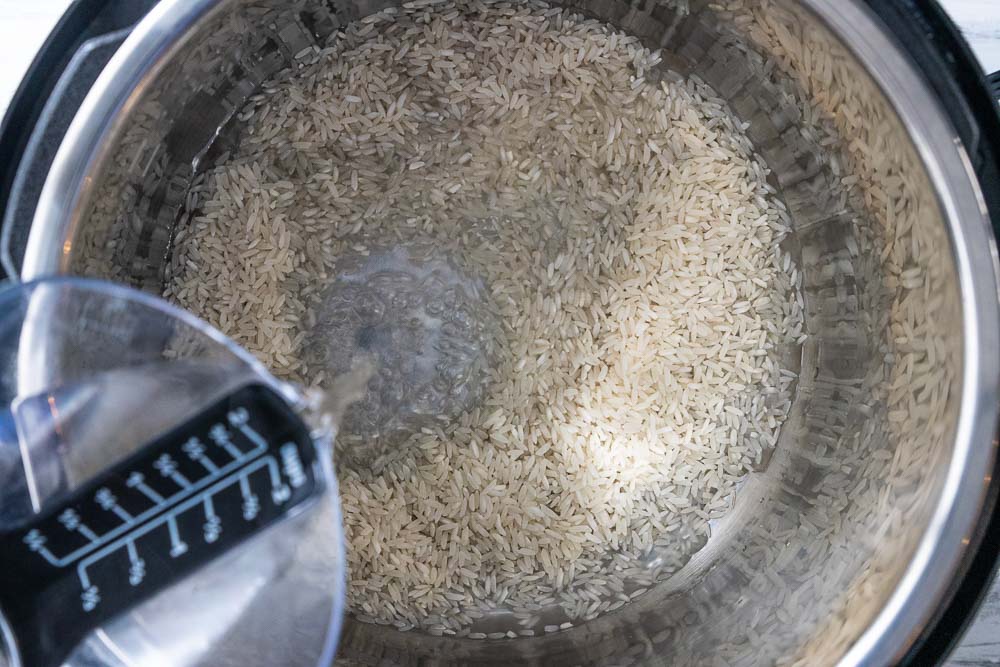 pouring water onto long grain white rice in an instant pot