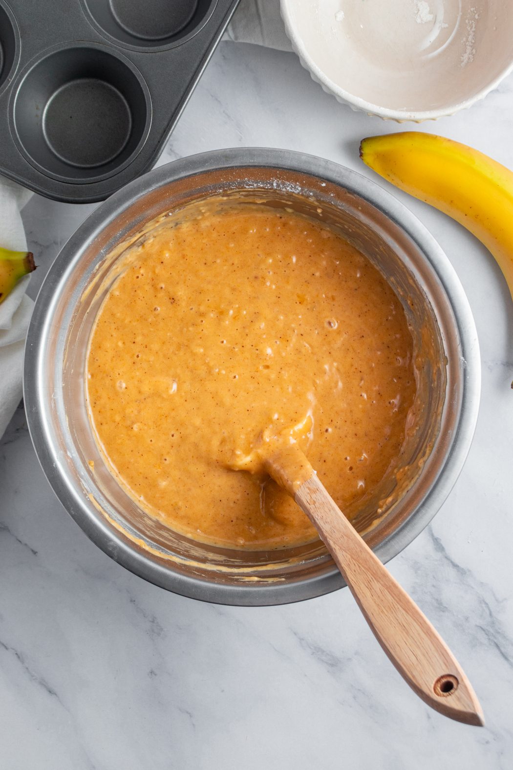 pumpkin banana muffin batter in a mixing bowl with a wooden spoon