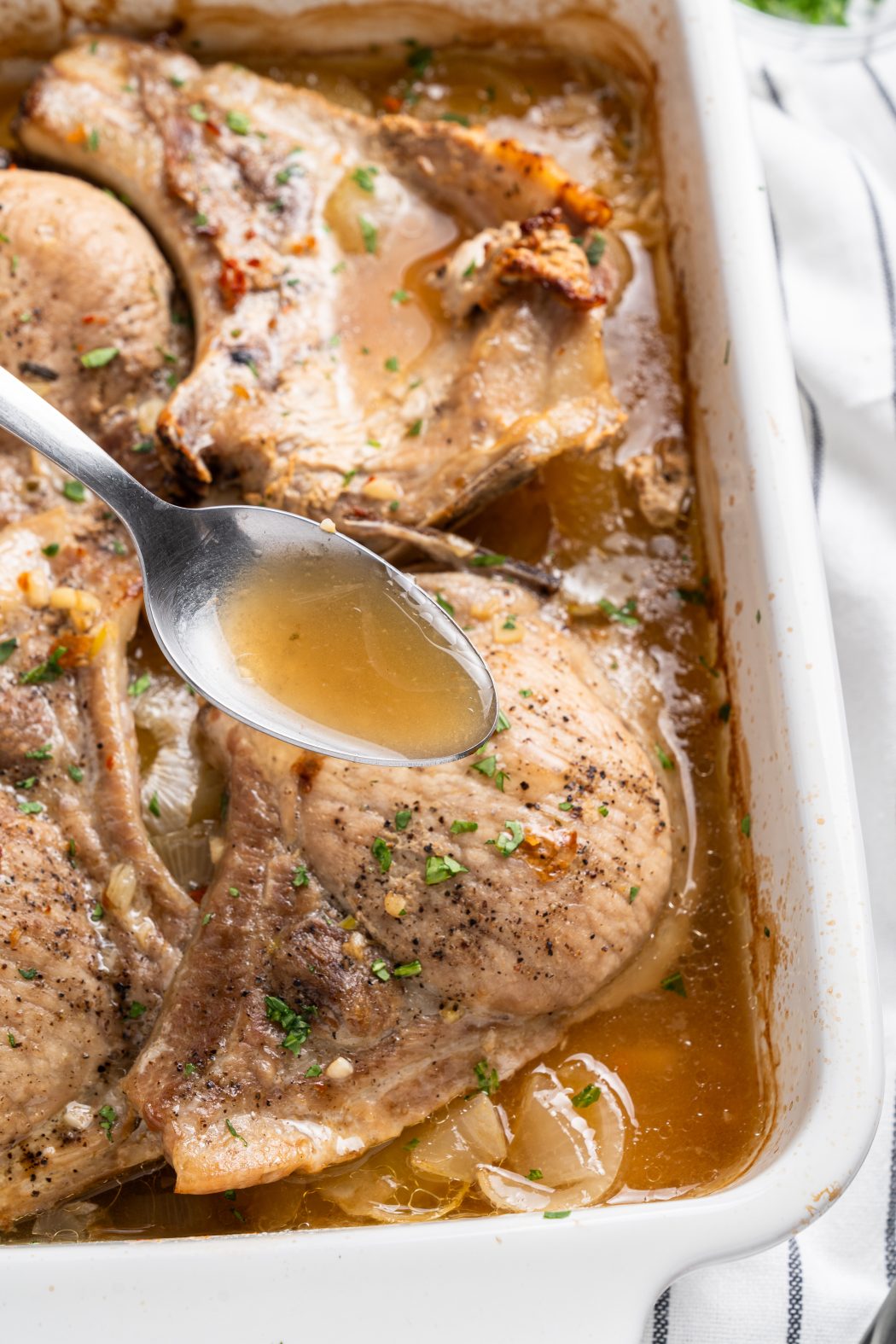baked pork chops and potatoes with a spoon that shows the broth