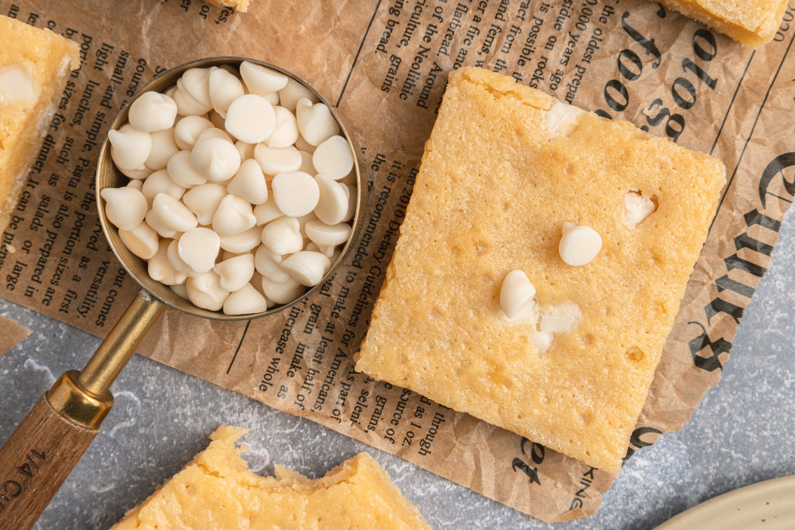 a cup of white chocolate chips by a white chocolate brownie